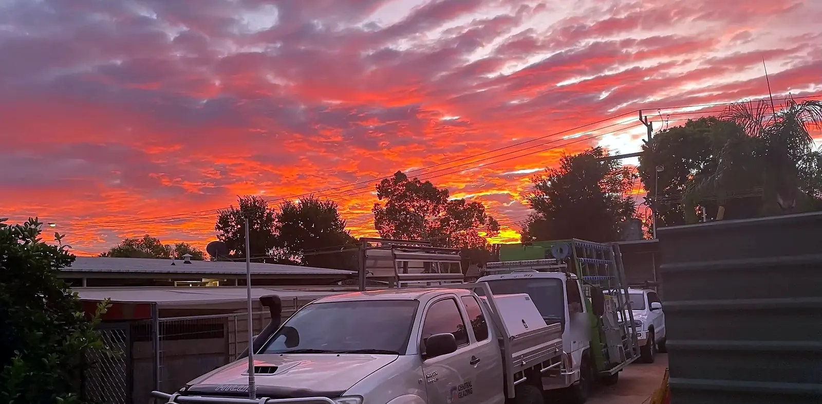 Central Glazing service ute and glass truck parked in a driveway under a red and orange sunset sky