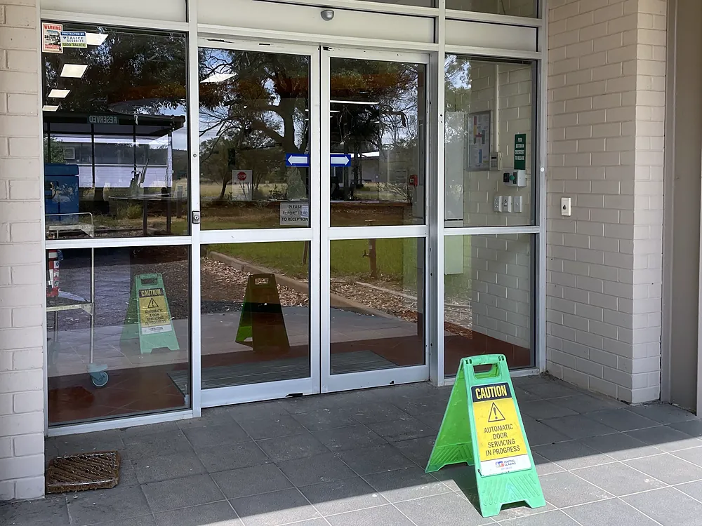Glass automatic entrance doors with a Central Glazing sign reading Caution, automatic door servicing in progress