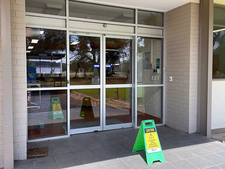 Glass automatic doors with a sign reading Caution, automatic door servicing in progress