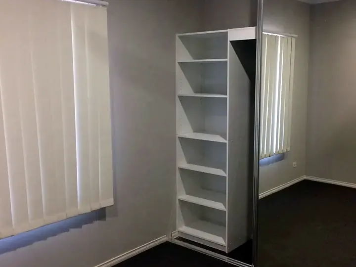 Mirrored sliding wardrobe doors in an empty bedroom beside a set of white shelves
