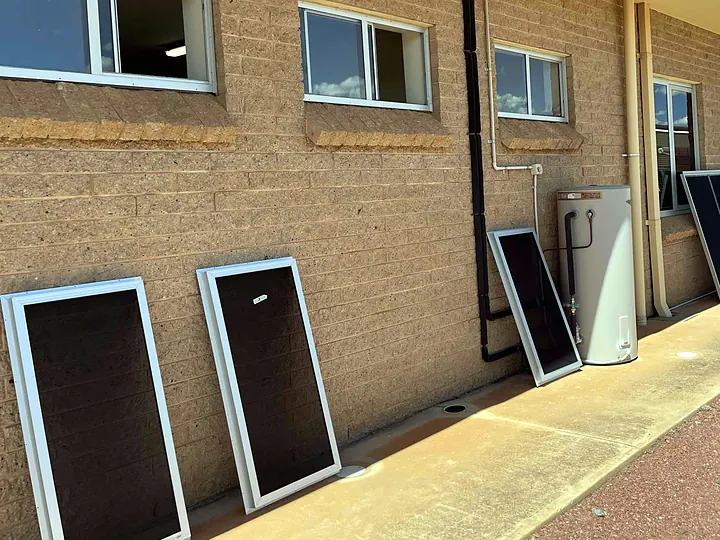 Framed window screens leaning against a brick wall beside the windows they are for
